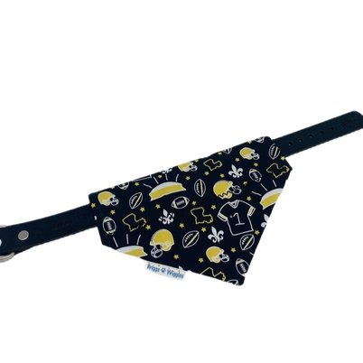 Flat lay of a reversible Saints-inspired dog bandana with details black and gold designs, including the Superdome, fleur-de-lis, footballs and Louisiana outline.