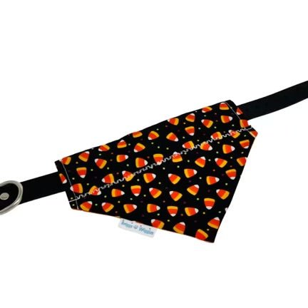 Flat lay of Candy Corn dog bandana with black background, floating candy corn pattern, and colorful polka dots, shown in collar slide style, handmade Halloween pet accessory.