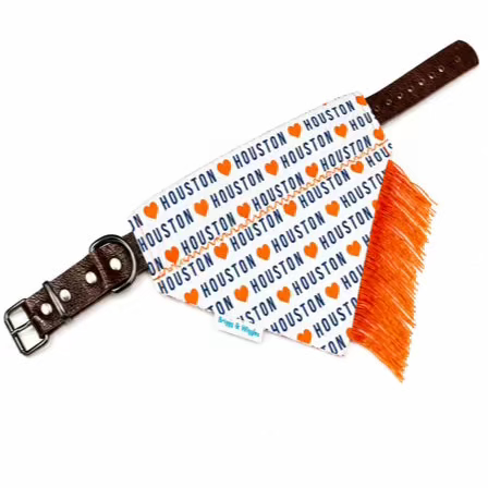 A dog bandana with a brown leather strap and a bright orange fringe, featuring a white background printed with the Houston Rockets logo in navy blue and orange.